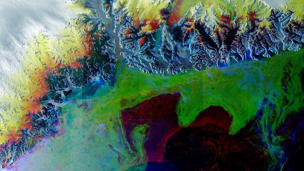 Satellite view of a Greenland outlet glacier flowing down to the sea, streaked with dark medial moraines