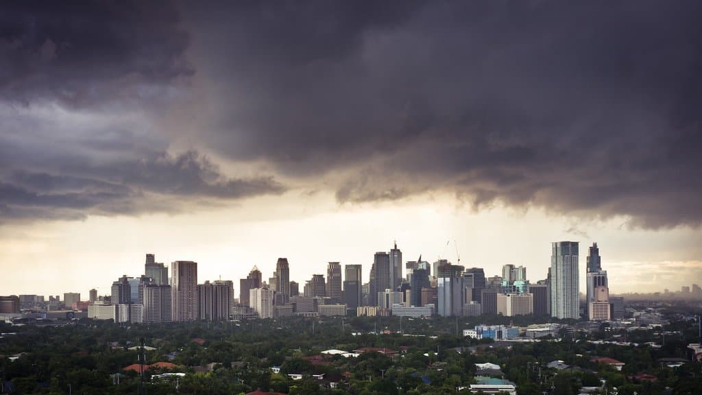 Dark, heavy storm clouds and rain over a East Asian city skyline.