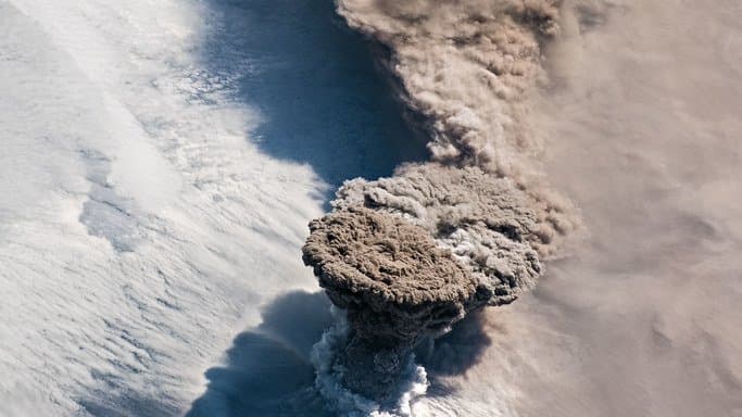 A satellite view of the Raikoke volcano erupting a tall plume of ash into the atmosphere.