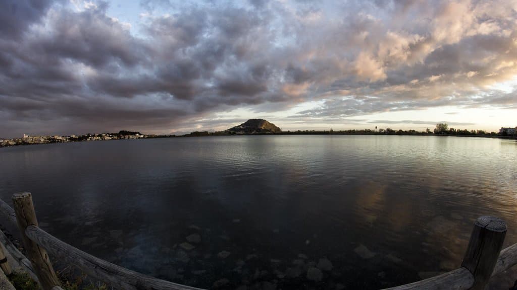 A volcanic crater lake in the Campi Flegrei at dusk, ringed by low wooded hills and a small town