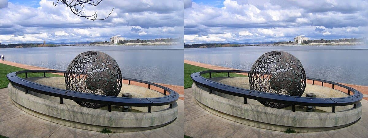 Two near-identical photographs placed side by side: a large open lattice globe sculpture on a curved stone plinth beside a lake, with a low pale public building and low hills on the far shore under a cloudy sky. Small details differ between the frames, including a bare branch that hangs into the sky at the top left of the left-hand image and is absent from the right-hand one.
