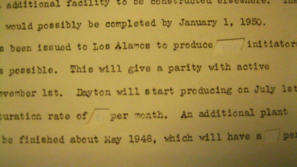 Close-up of a typewritten 1940s memorandum in which several words have been physically cut out of the paper, leaving blank slots in the middle of sentences about production schedules.