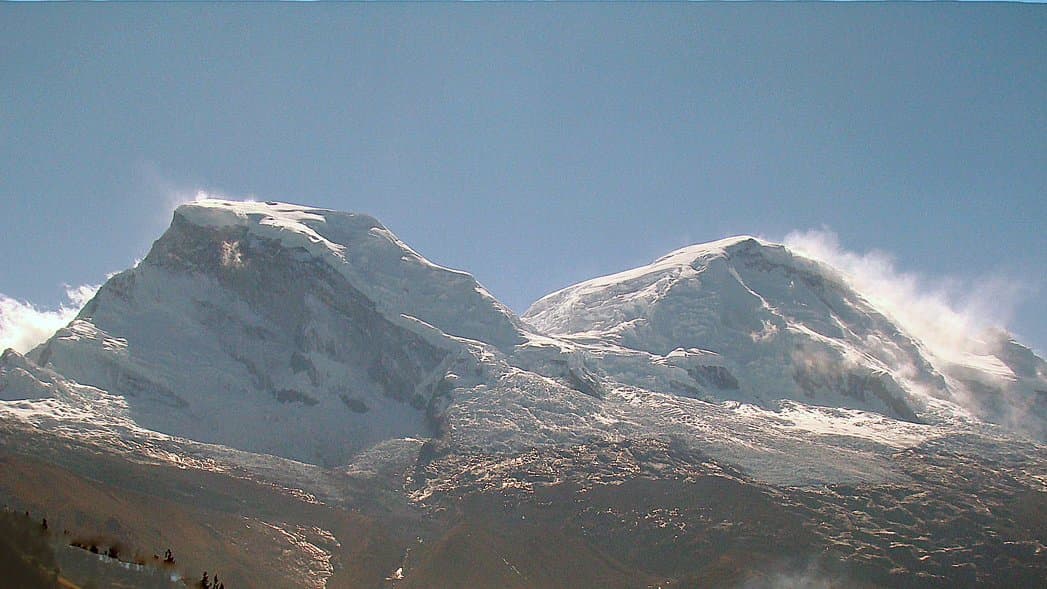 The twin snow-covered summits of Nevado Huascaran rising above brown ridges in Peru's Cordillera Blanca, seen from the Cordillera Negra.