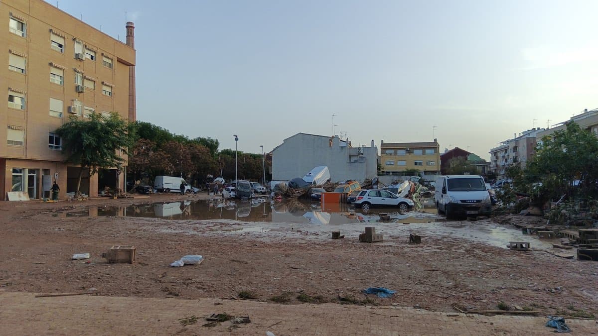 A mud-covered street in Paiporta near Valencia the day after the October 2024 flash flood, with cars shoved into piles, standing brown water and debris across the roadway