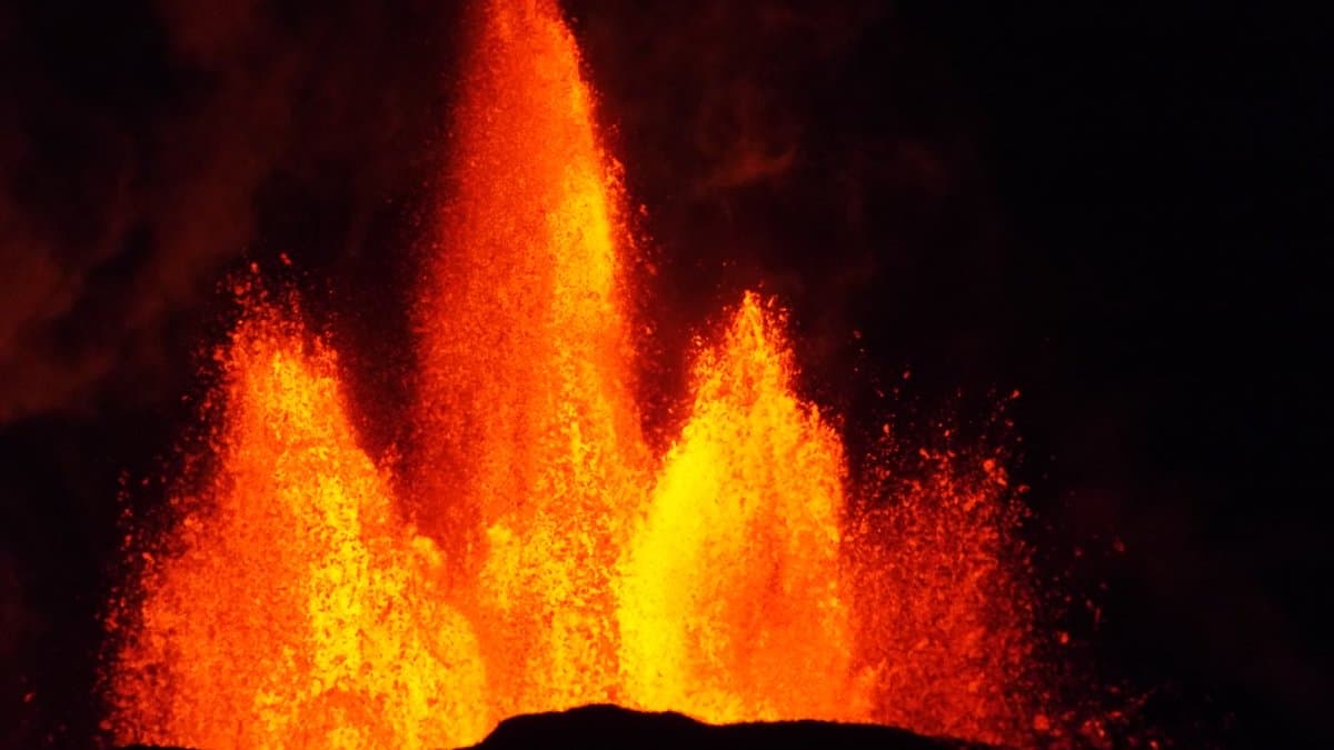 Bright orange lava fountains jetting upward from a fissure against a black night sky.