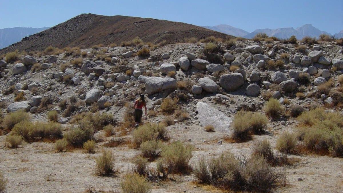 A low, boulder-strewn earthquake fault scarp crossing arid valley floor near Lone Pine, California, with a person standing at its base for scale and desert ranges behind