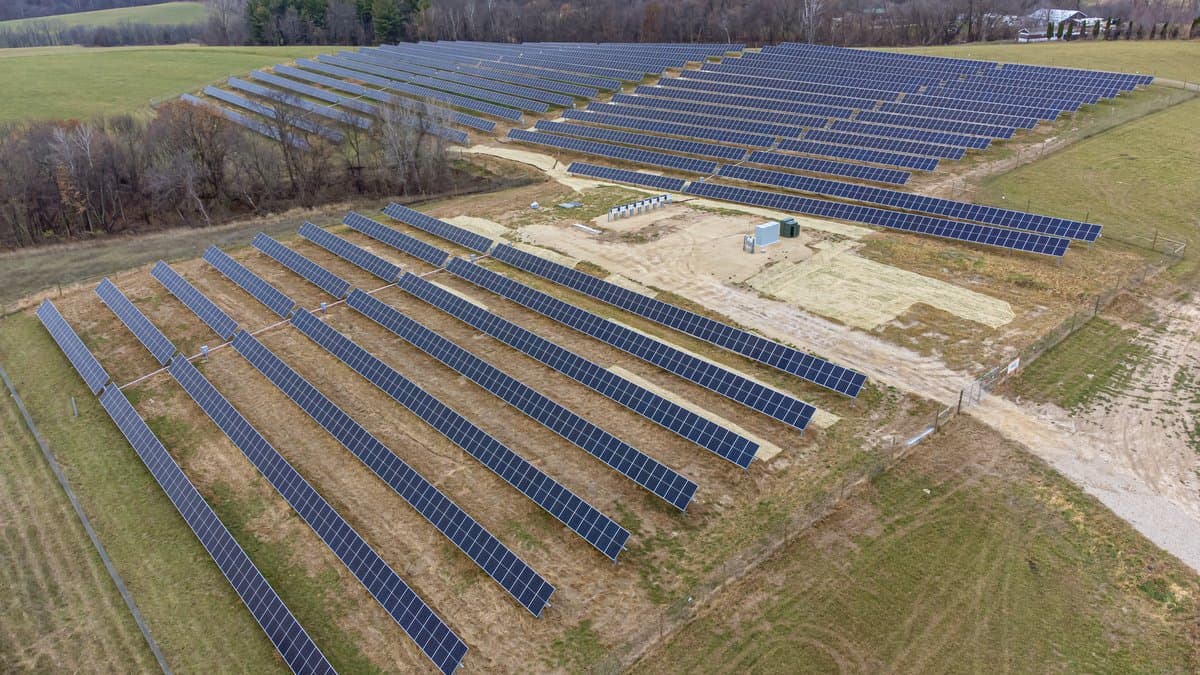 Aerial view of long rows of solar photovoltaic panels covering a field in Wisconsin, bordered by green pasture and treelines