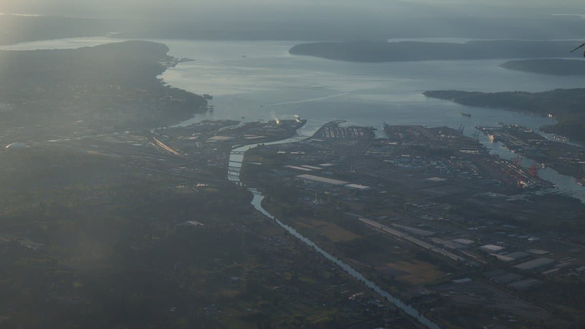 Elevated aerial view across downtown Tacoma and the low-lying Commencement Bay tide flats, with the Puyallup River channel and port terminals meeting the water of Puget Sound