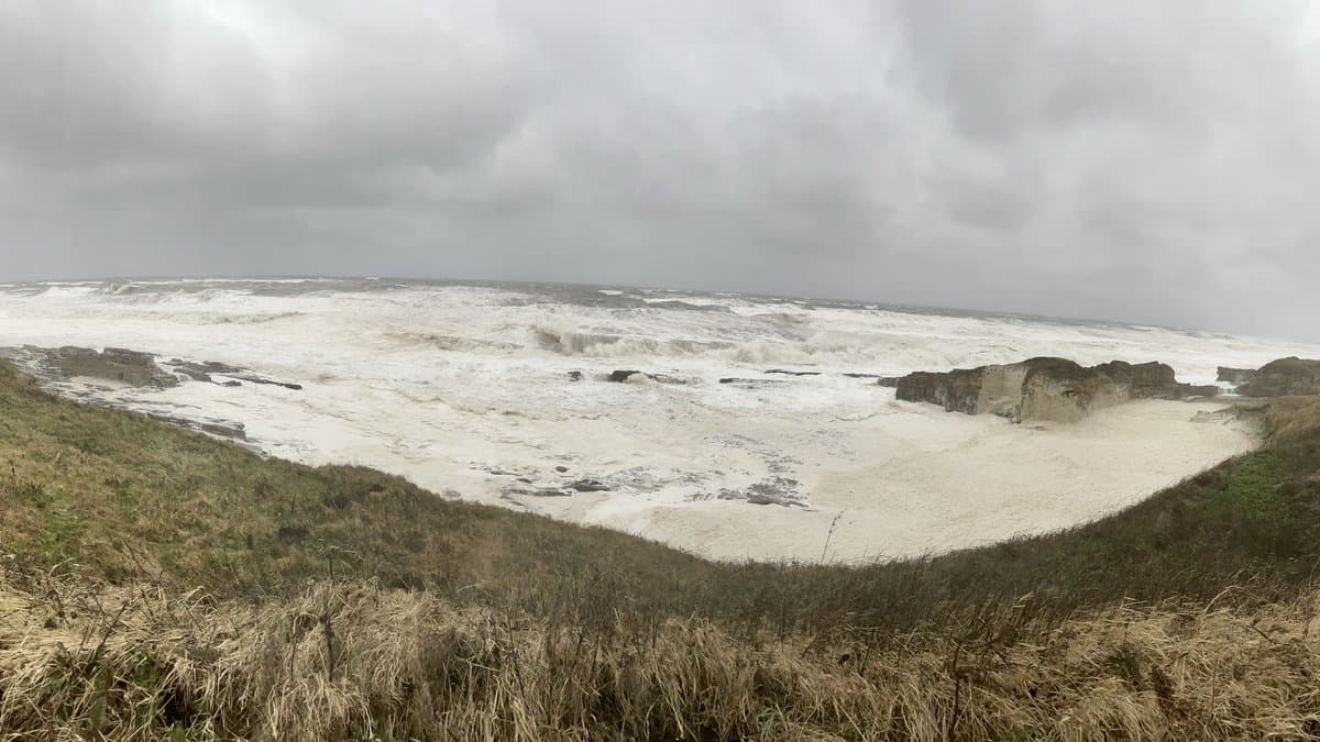 Storm waves and thick foam filling a rocky cove under a heavy grey sky on the Northumberland coast