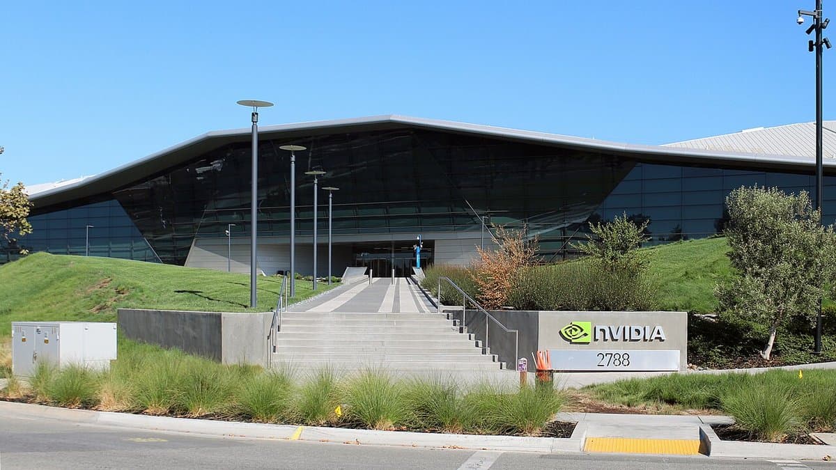 A low, angular office building with a dark faceted glass roof behind a grass bank, a wide flight of steps and a kerbside sign reading NVIDIA 2788.