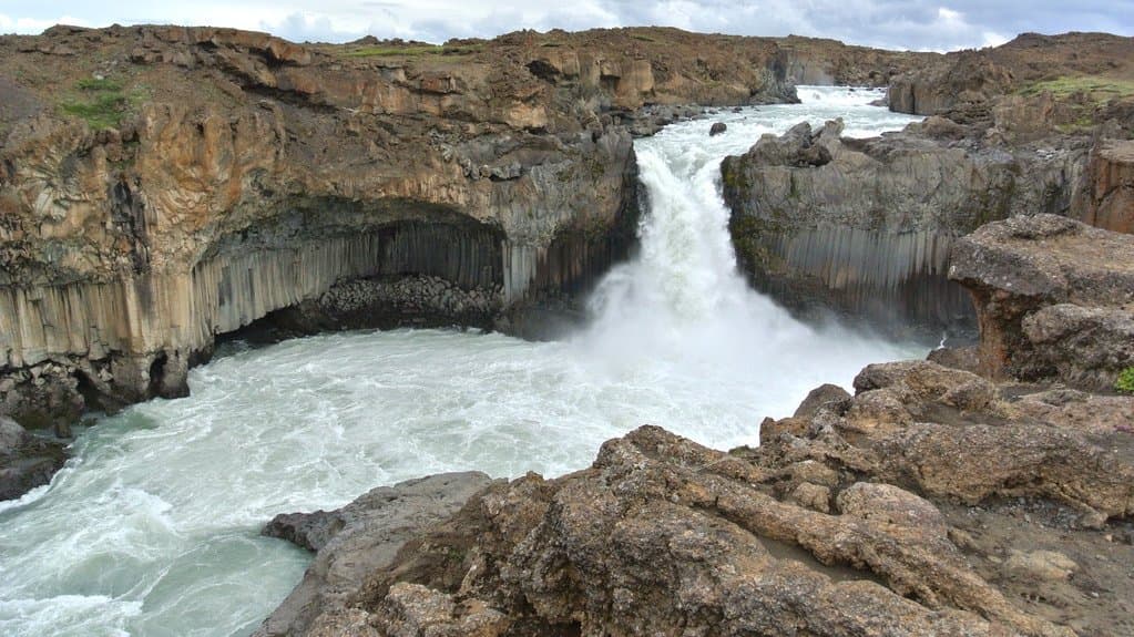 A river pouring over a waterfall between walls of dark hexagonal basalt columns.
