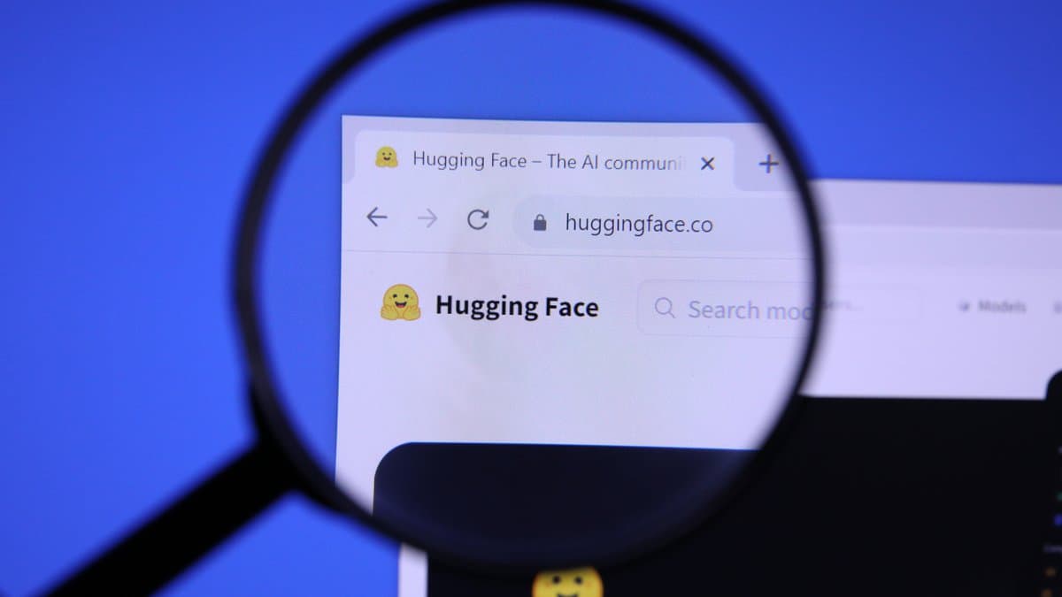 A magnifying glass held over a computer screen showing the Hugging Face website home page and its logo.