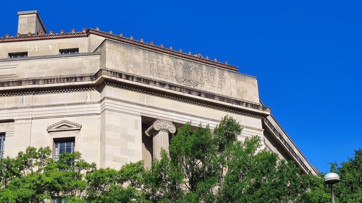The upper facade and carved stone relief of the Robert F. Kennedy Department of Justice Building in Washington, D.C., against a clear blue sky.