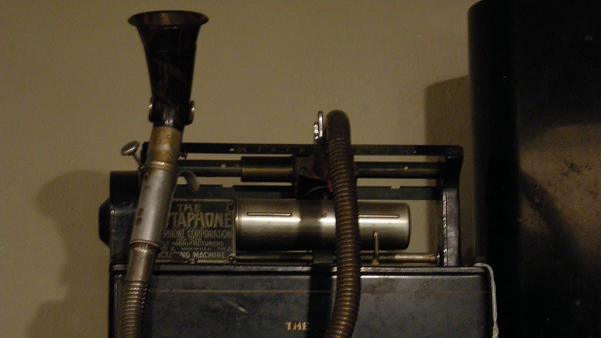 An early Dictaphone wax-cylinder dictating machine with a speaking horn and flexible tube, photographed in a museum display.