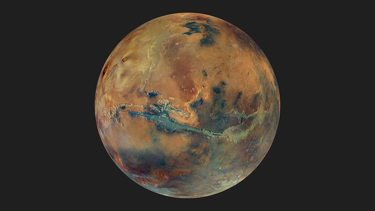 Full globe of Mars in colour, centred on the Valles Marineris canyon system, with dark basaltic sand regions and lighter dust-covered highlands.