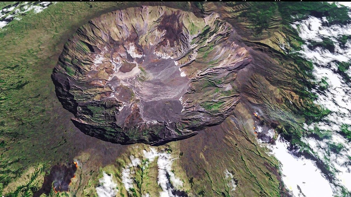 Oblique satellite view of the broad summit caldera of Mount Tambora on the island of Sumbawa, Indonesia, with cloud over the surrounding green slopes.