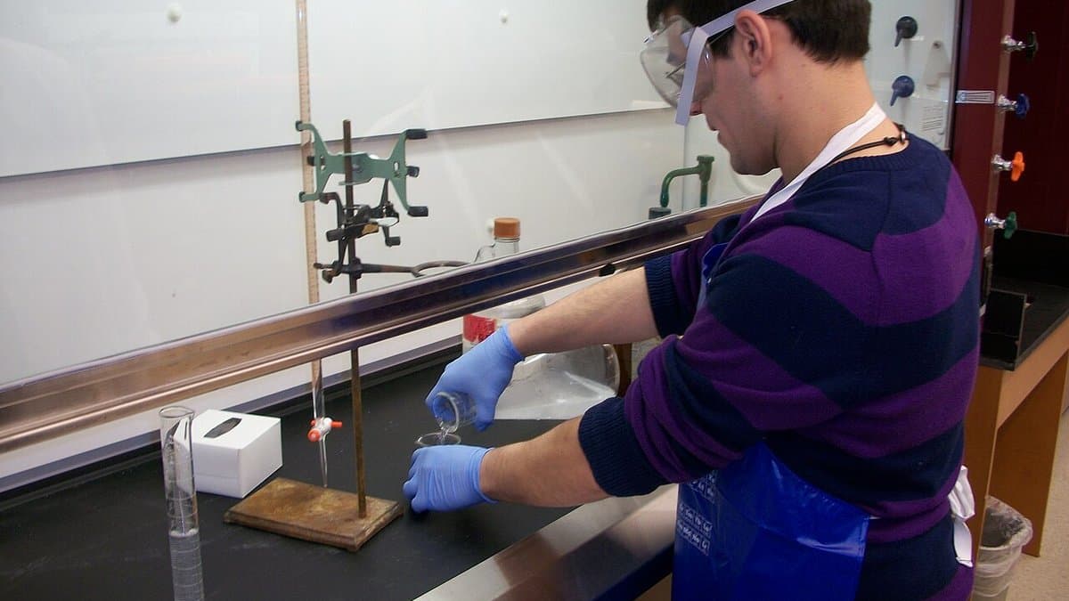 A chemist in a laboratory working with glassware inside a fume hood