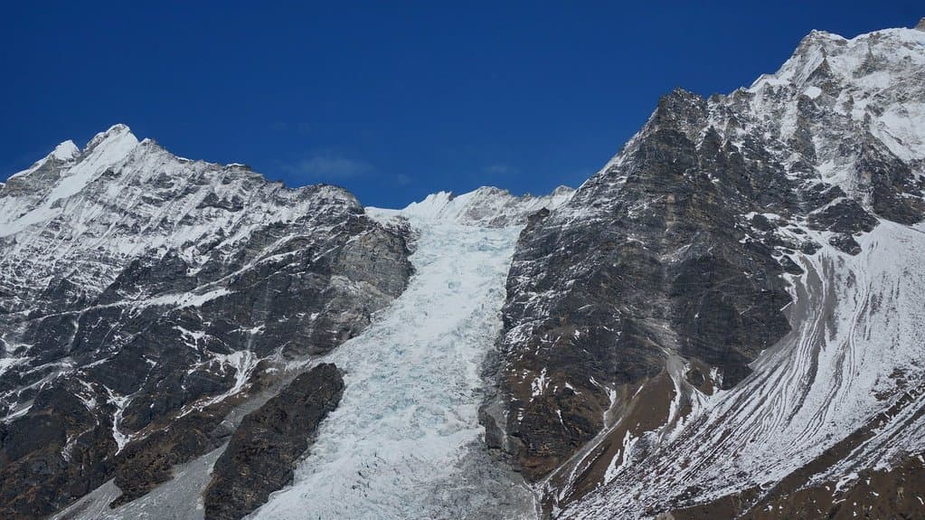 A steep icefall of a hanging glacier spilling between dark rock buttresses on a snow-covered flank of the Langtang Lirung massif in Nepal.
