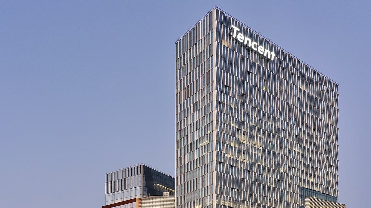 The upper floors of Tencent's Binhai headquarters tower in Shenzhen at dusk, the company name lit in white letters across the top of the glass facade against a clear blue sky.