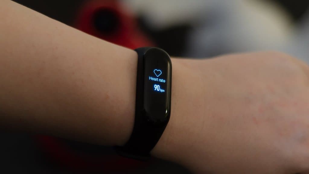 A black fitness band worn on a wrist, its small screen showing a heart symbol and the reading 'Heart rate 90 bpm'.
