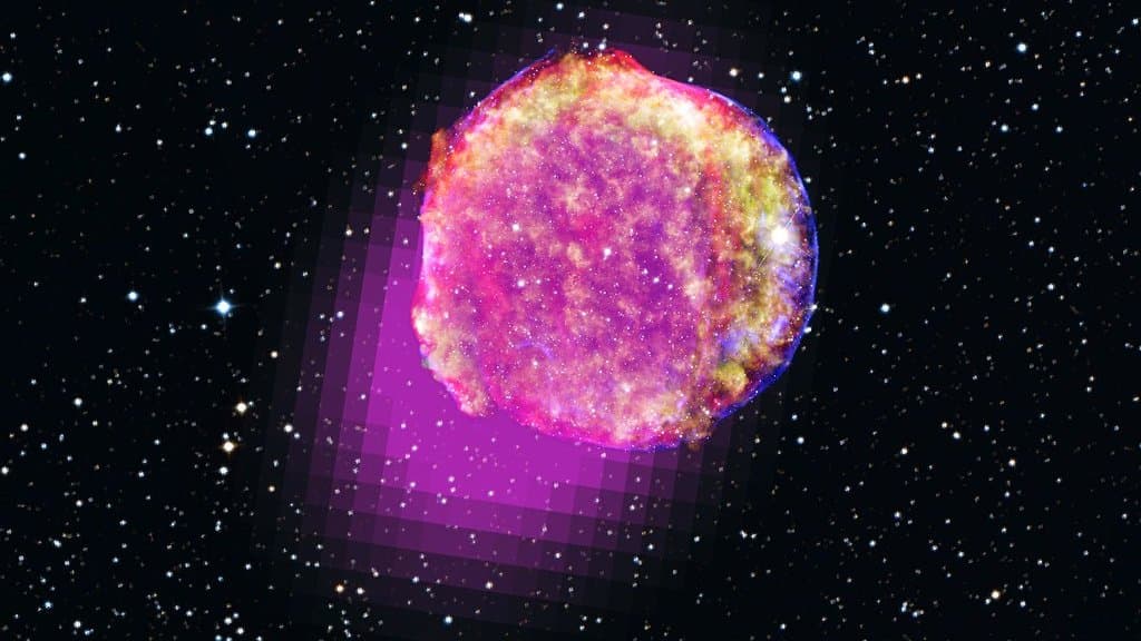 The shell of Tycho's supernova remnant, a round cloud of pink and gold X-ray emission against a dense starfield, with a blocky magenta patch of gamma-ray emission behind it.