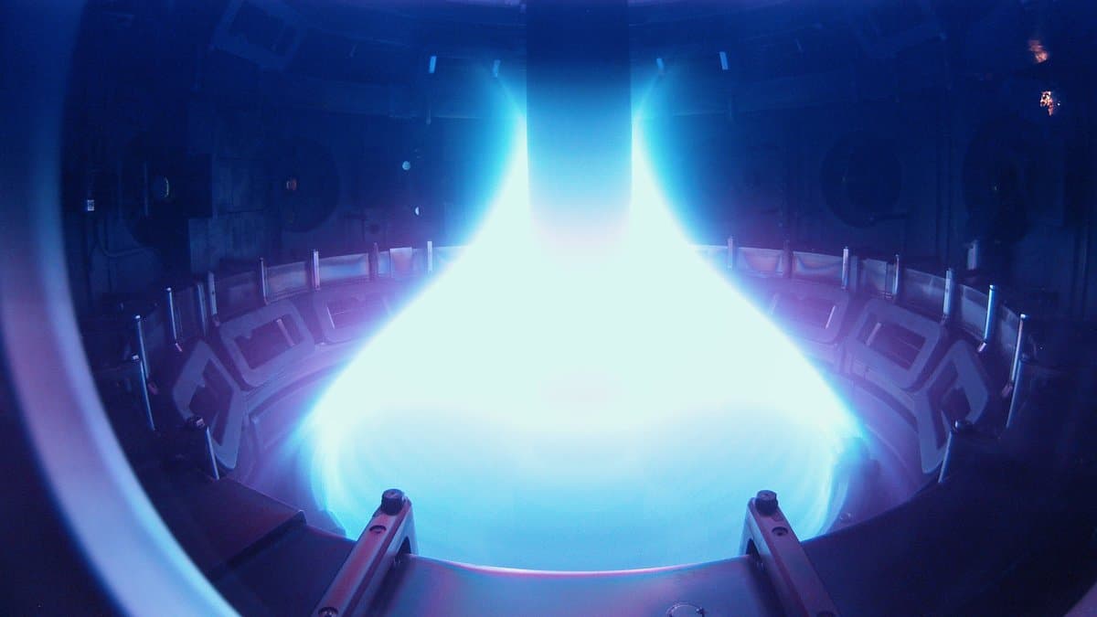 Interior of the MAST spherical tokamak during a shot: a bright blue-white plasma fills the round vacuum vessel, with metal divertor plates and support struts visible around it.