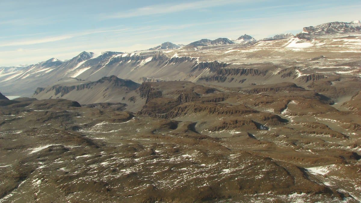 Aerial view of the Labyrinth in Wright Valley, one of Antarctica's ice-free McMurdo Dry Valleys: bare brown soil and rock ridges streaked with snow, with mountains on the horizon.