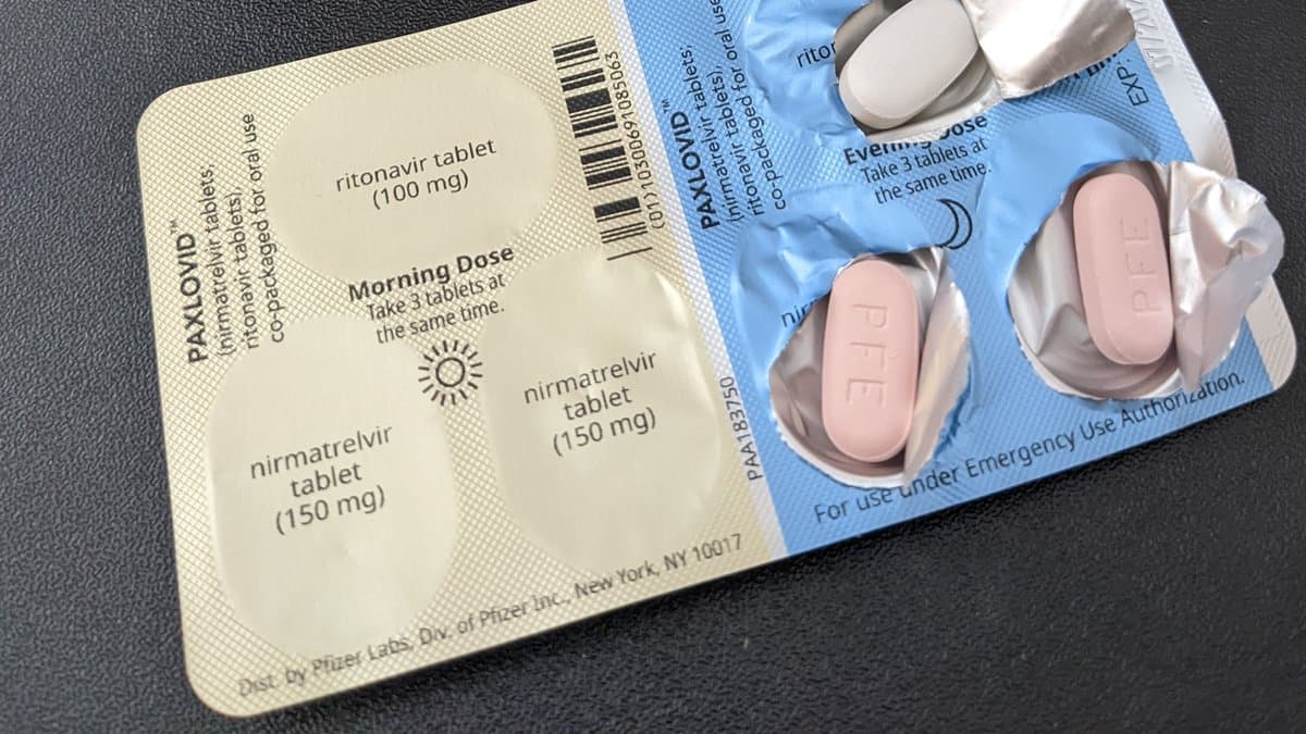 An opened Paxlovid blister card and carton, showing two pink nirmatrelvir tablets and a white ritonavir tablet in morning-dose and evening-dose panels.
