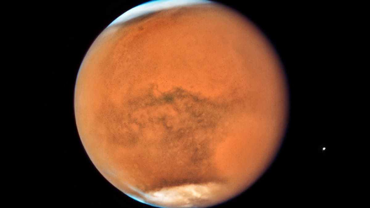 Full disc of Mars seen from space, its surface veiled in orange dust during the 2018 planet-encircling dust storm, with a bright white south polar cap and a thin blue haze along the limb.