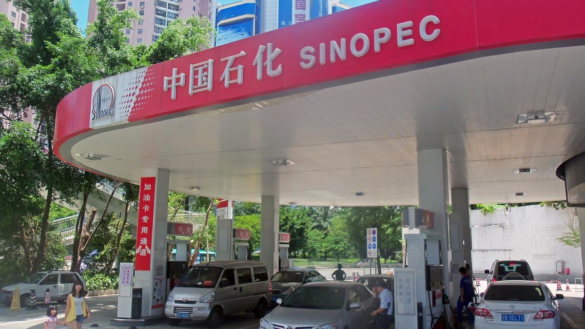 Cars refuelling beneath the red canopy of a Sinopec petrol station in Shenzhen, China, with high-rise blocks behind