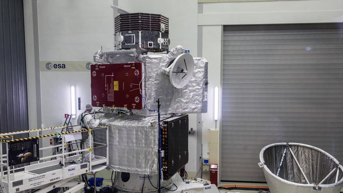 The assembled BepiColombo spacecraft stack in an ESA clean room: the silver Mercury Transfer Module at the bottom, mounted on a cone-shaped adapter; the Mercury Planetary Orbiter, with a dark red cover panel, in the middle; and JAXA's Mercury Magnetospheric Orbiter on top, with an engineer in a white clean-room suit working alongside