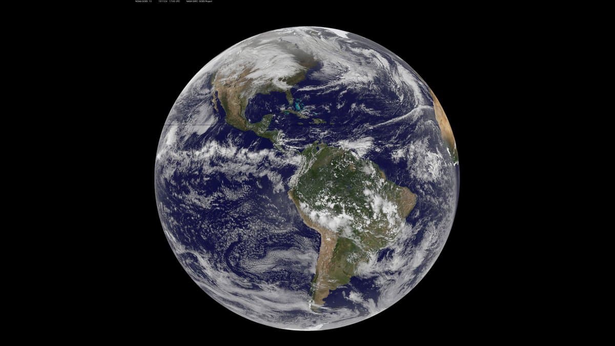 Full-disk view of Earth from the GOES-13 geostationary weather satellite, the Americas centred beneath swirling white cloud bands over dark blue ocean, against black space.