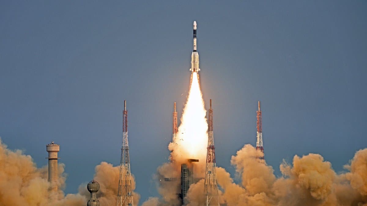 An Indian GSLV rocket climbs above its launch pad on a bright exhaust plume, with lightning towers and billowing smoke below it.