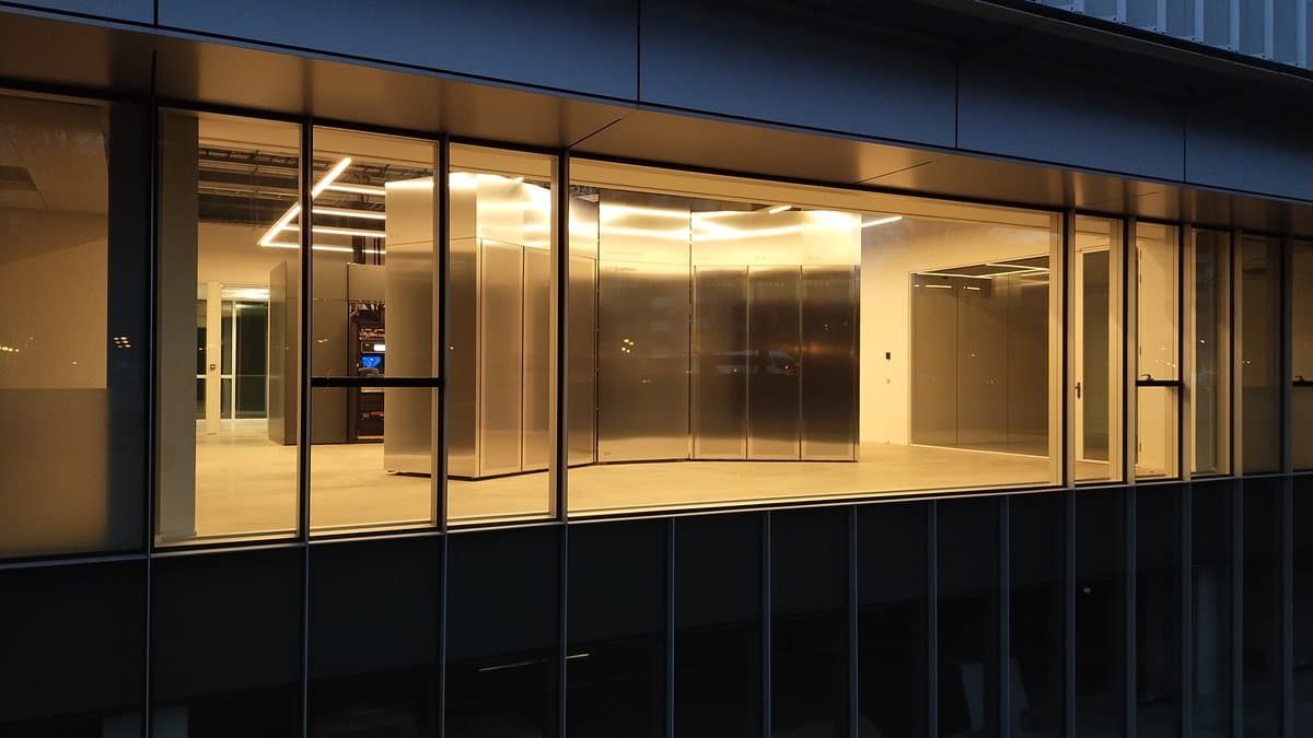 A large stainless-steel IBM Quantum System Two enclosure standing in a brightly lit hall, seen at dusk through the glass facade of a modern research building.