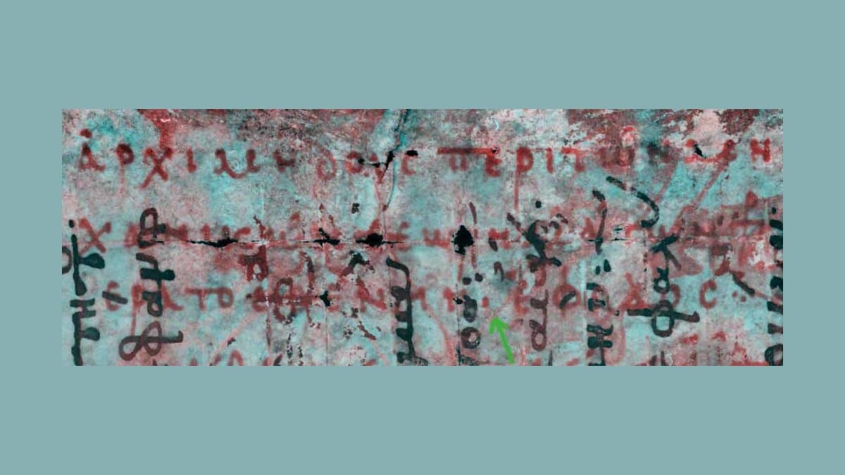 Multispectral image of a page of the Archimedes Palimpsest: red Greek letters of the erased Archimedes text run left to right across the page, crossed at right angles by darker letters of the medieval prayer book written over them. A small green arrow marks one point in the recovered text.