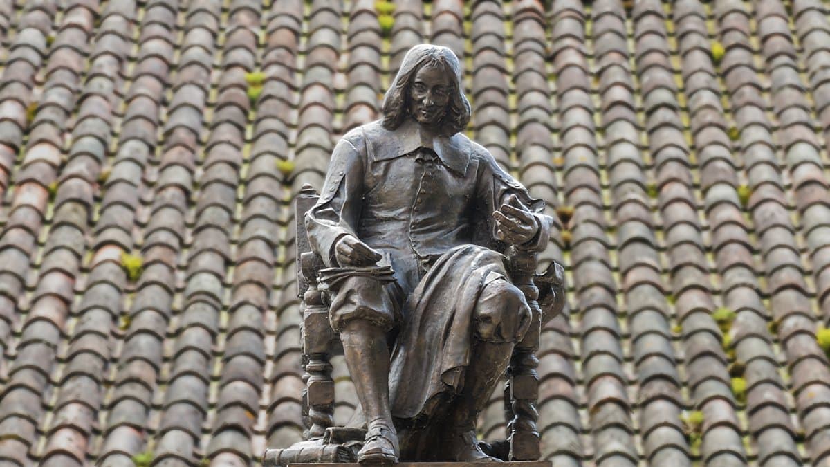 Bronze statue of the seated 17th-century mathematician Pierre de Fermat against a terracotta tiled roof