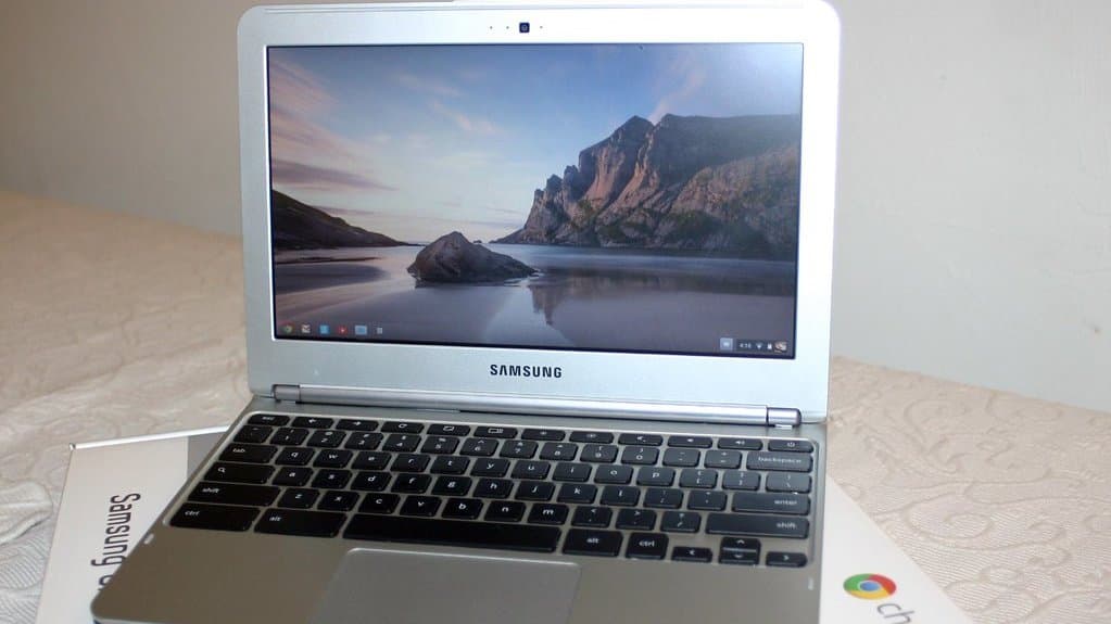 A silver Samsung Chromebook laptop, open and switched on, resting on its box, which carries the Google Chrome logo.