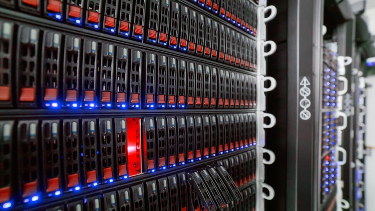 Rows of rack-mounted servers receding down a data-centre aisle, with blue status lights along each row of drive bays and one red drive carrier.