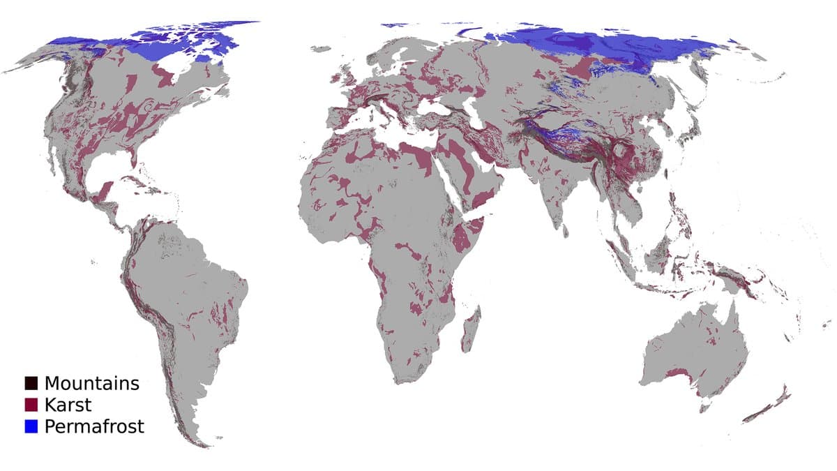 World map with land in grey, showing karst regions in dark red across the Mediterranean, the eastern United States, southern China and Southeast Asia, and permafrost in blue across northern Russia, Canada and Alaska, with mountain areas in black.