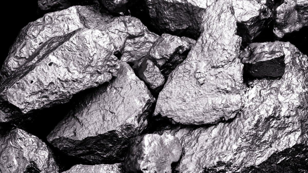 Close-up photograph of chunks of silvery-grey manganese metal filling the frame against a black background.