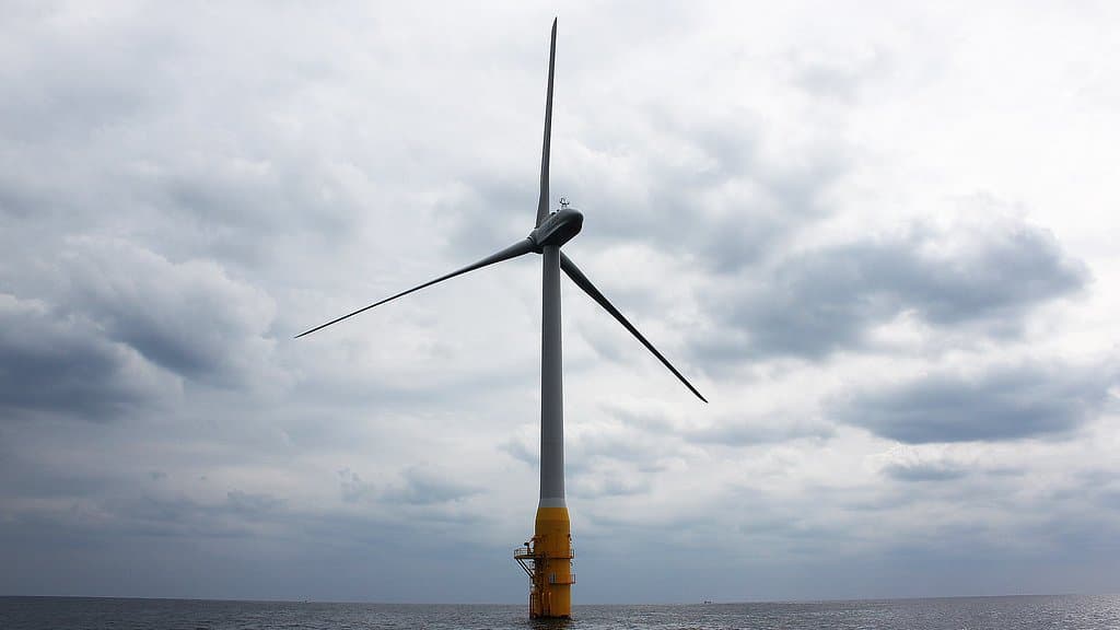 A single floating offshore wind turbine standing in open sea, its yellow cylindrical float visible at the waterline beneath a heavy grey sky.
