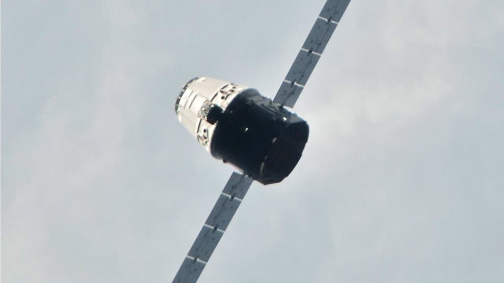 A Dragon cargo capsule with extended solar arrays, seen at close range from the International Space Station.