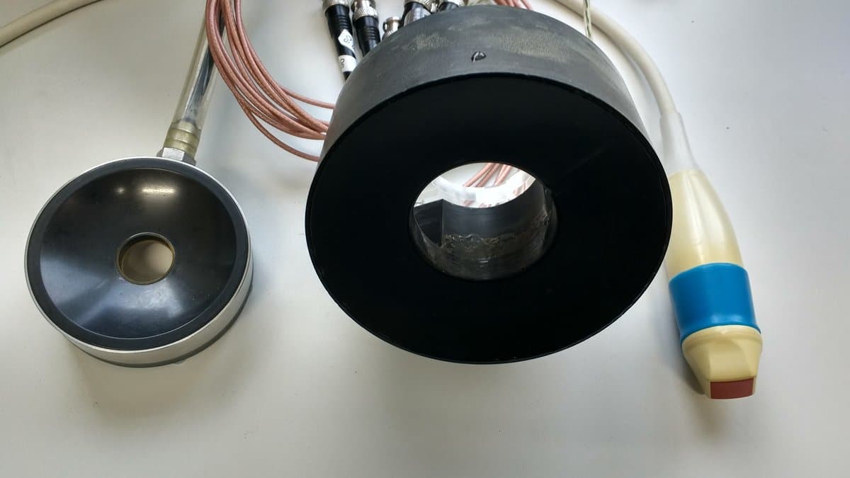 Two bowl-shaped focused ultrasound transducers with coaxial cables on a white bench, next to a handheld cardiac ultrasound imaging probe.