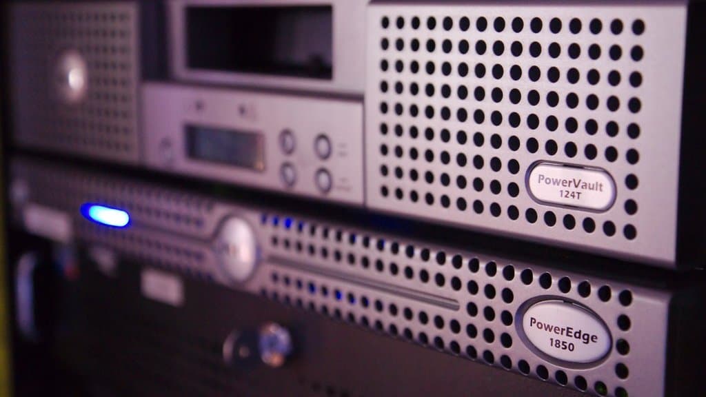 Close-up of rack-mounted servers, with a tape library unit above and a 1U server with lit status indicators below.