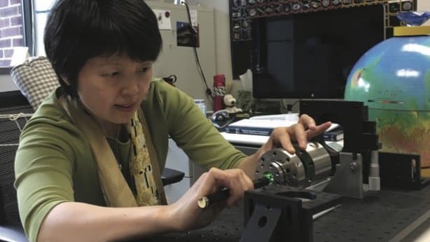 A researcher aligns a green laser into a diamond anvil cell mounted on an optical bench.