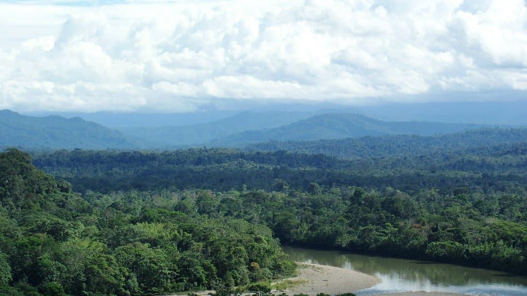 Dense tropical rainforest canopy stretching to forested ridges, with a broad sky of clouds above