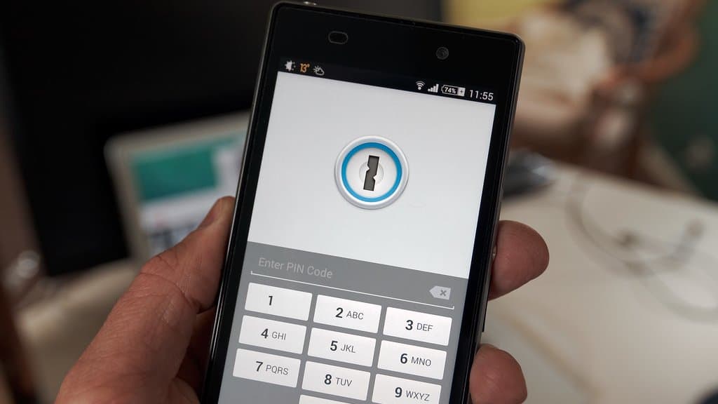 A hand holds an Android phone showing a password manager app locked behind a PIN keypad.