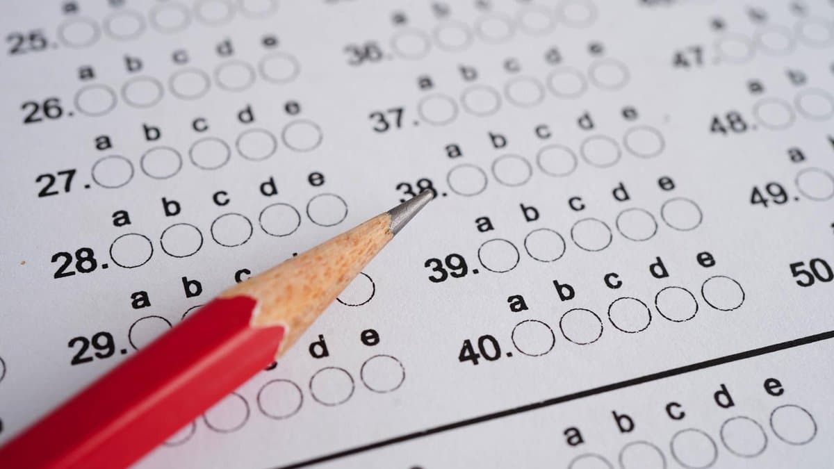 Close-up of an unmarked multiple-choice answer sheet, rows of lettered options a through e in blank circles, with a red pencil lying across the page.