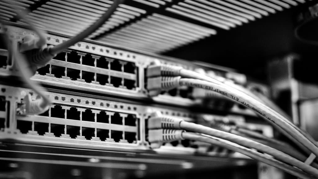 Two rack-mounted Cisco network switches in a data center, their ports filled with patch cables, in black and white.