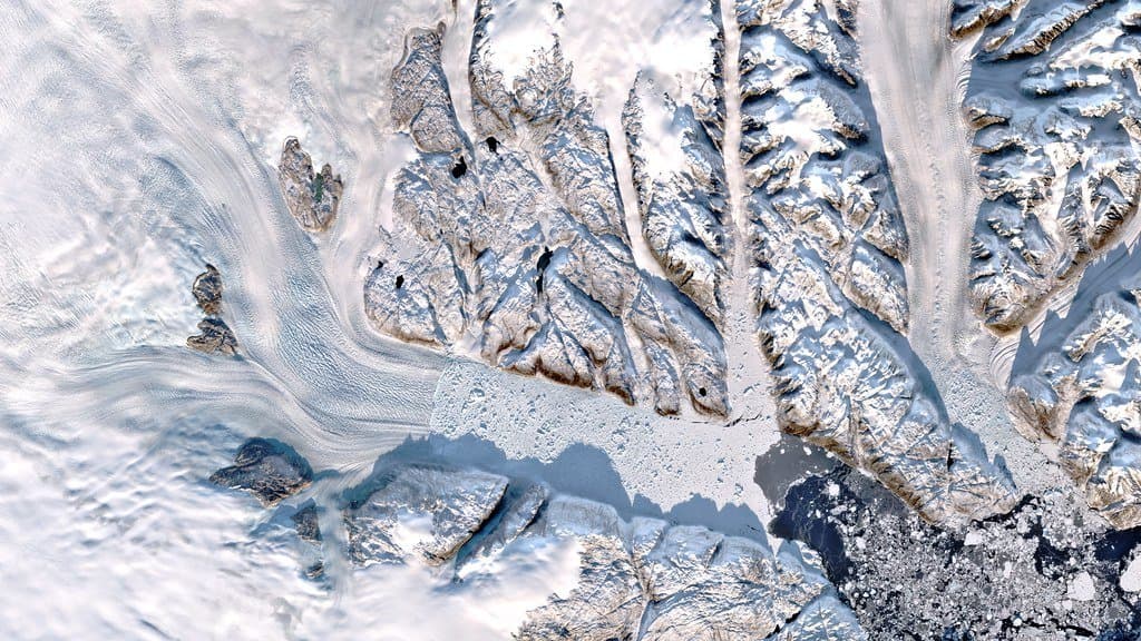 Satellite view of Helheim Glacier in southeast Greenland, its flow lines running down the glacier tongue into a fjord filled with broken ice